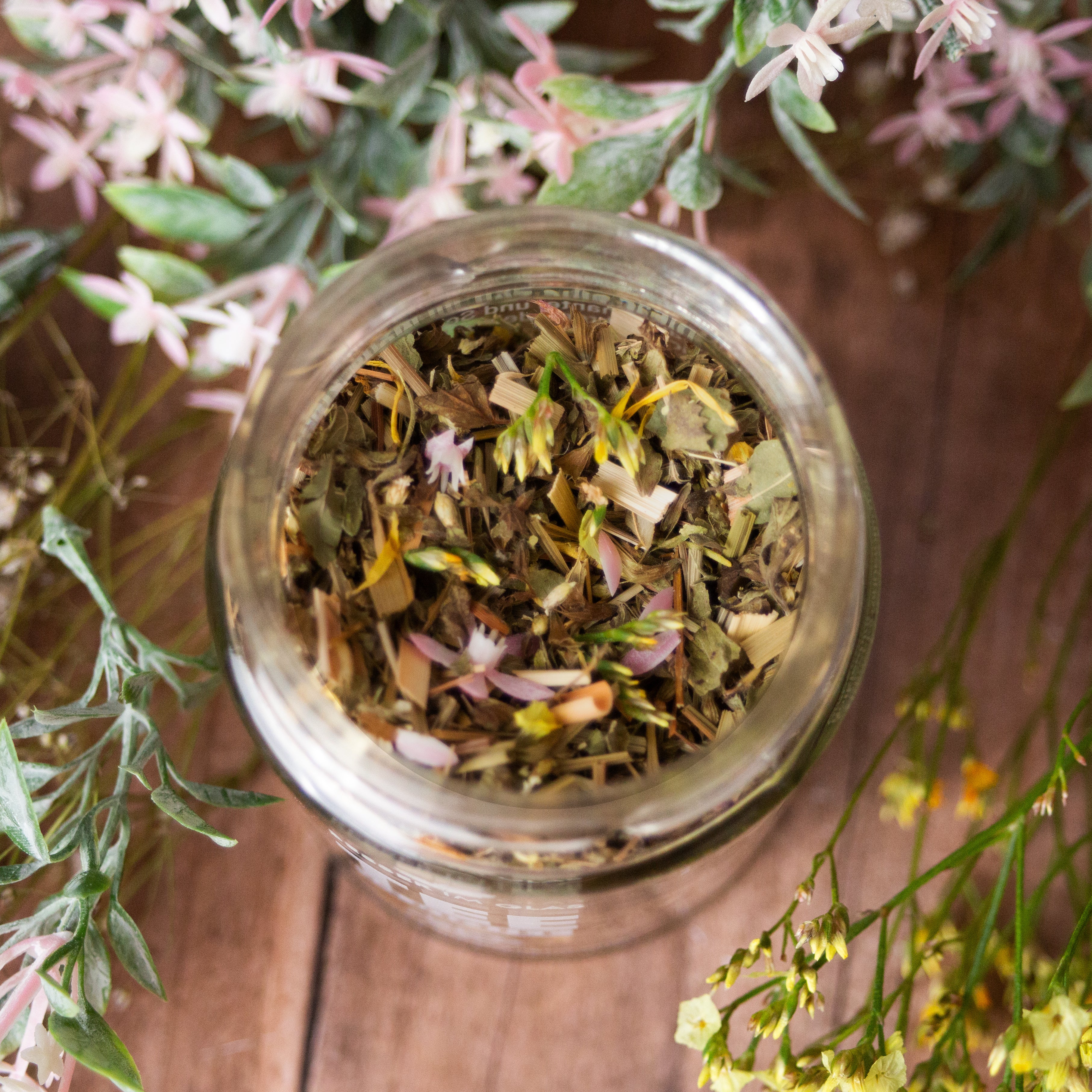 Loser bio Kräuter Tee im Glas. Bio-Kräutertee aromatisiert mit Grapefruit- und Limettengeschmack. Der Tee enthält Bio-Melisse, Bio-Zitronengras, Bio-Schafgarbenkraut, Bio-Rosmarin, Bio-Karotte, Bio-Kamille, Bio-Spirulina, Bio-Frauenmantel, Bio-Süßkraut, Bio-Ringelblumenblüten, Bio-Rotkleeblüten, natürliches Grapefruitaroma und Limettenöl. Das Tee Glas ist umgeben von Blumen. Bio Tee ohne Zucker.