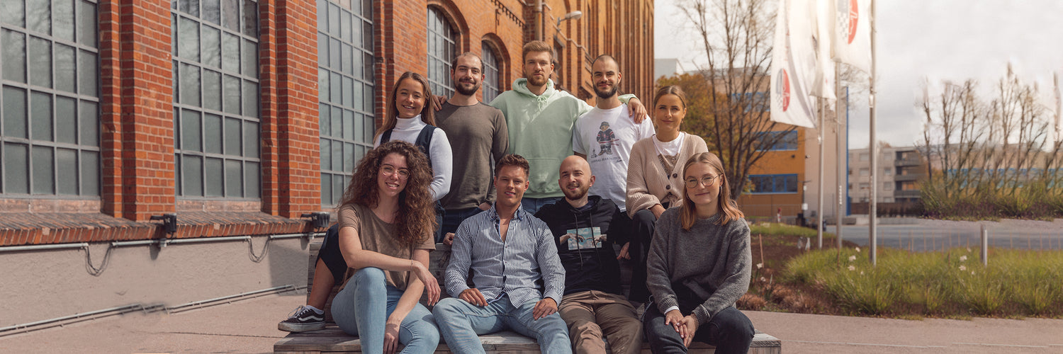 Das junge Startup-Team sitzt lächelnd gemeinsam auf einer Bank
