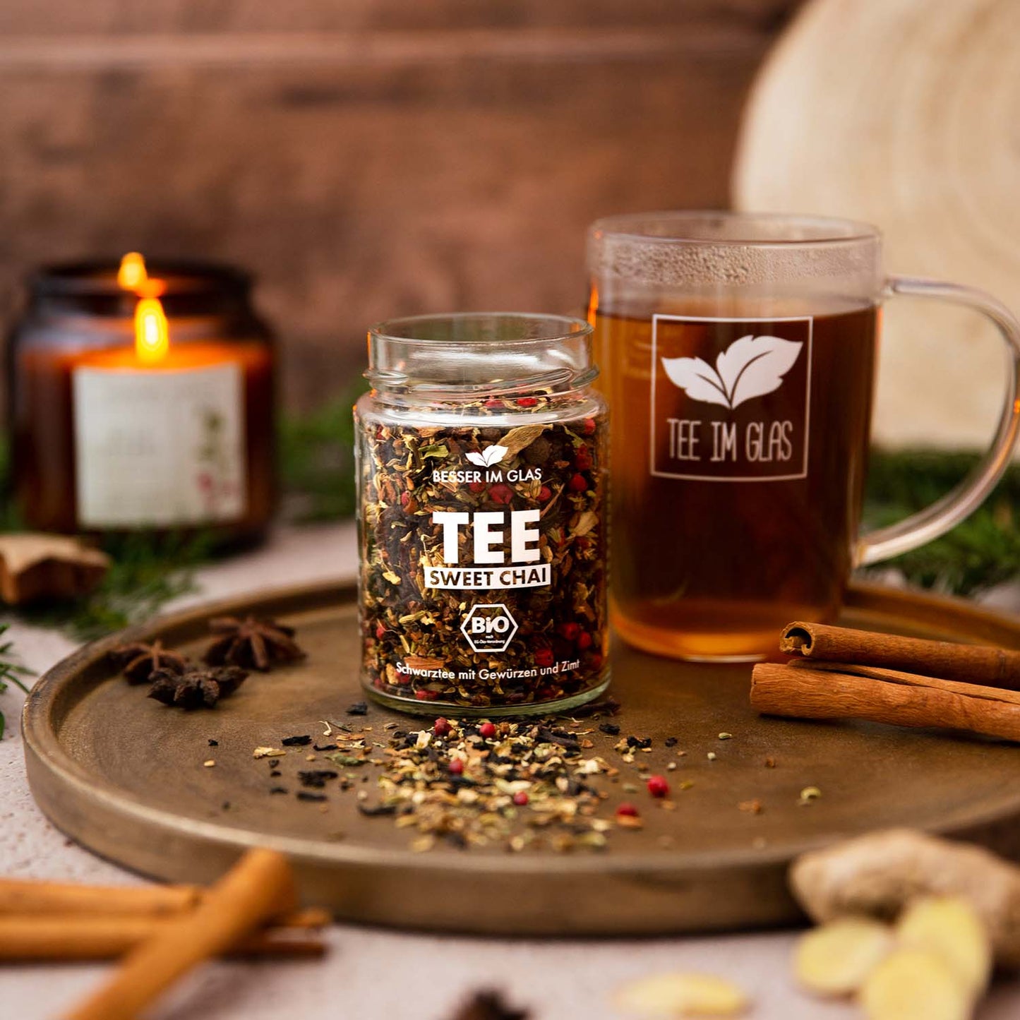 Loser bio sweet Chai Tee im Glas. Mischung aus Bio Gewürzen, Bio Kräutern und Bio Schwarzem Tee mit Kardamom- und Vanillearoma. Das Tee Glas ist umgeben von Zimt und frischem Ingwer. Außerdem ist eine Teetasse zu sehen. In dem Teeglas mit Henkel befinden sich der Sweet Chai Tee. Bio Tee ohne Zucker.