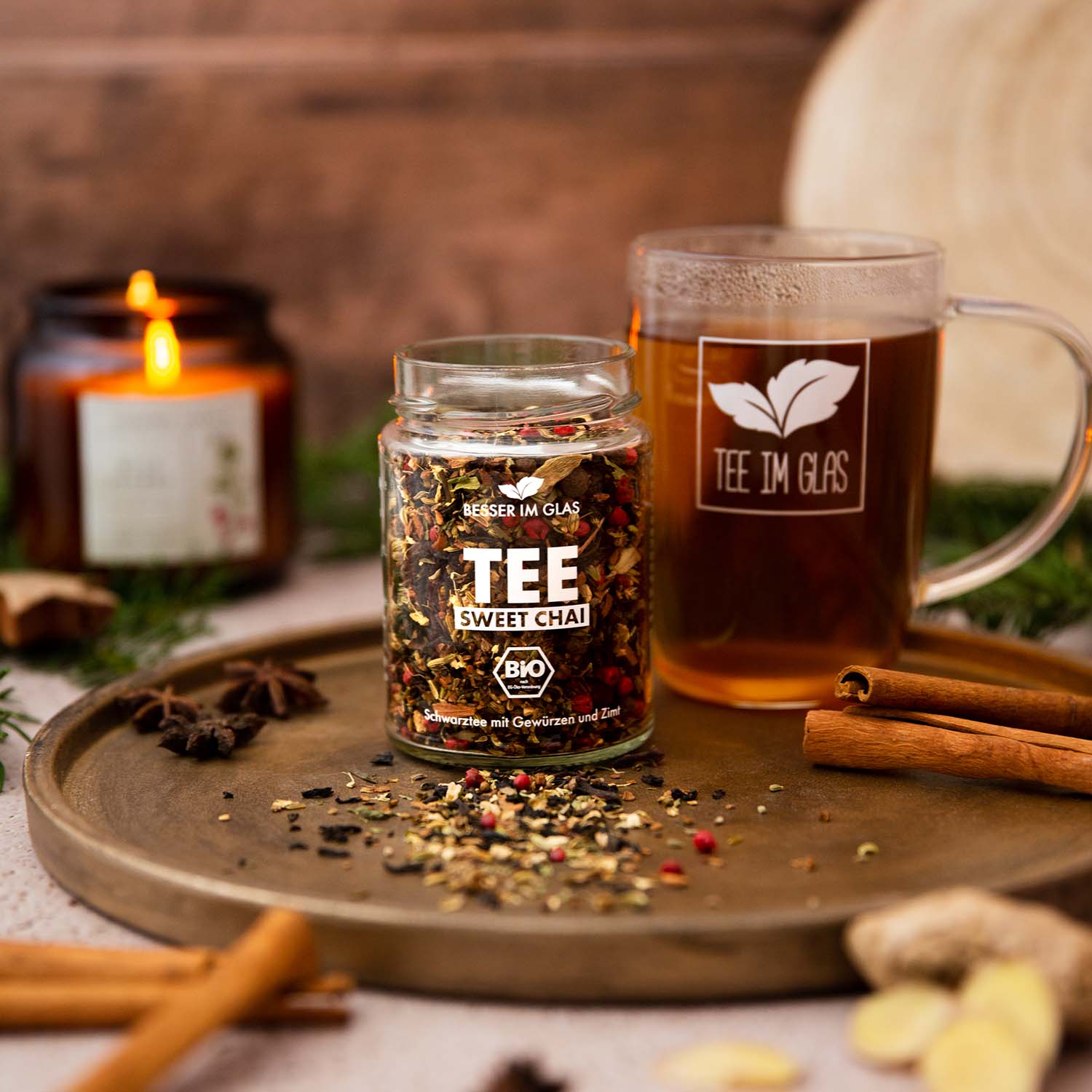 Loser bio sweet Chai Tee im Glas. Mischung aus Bio Gewürzen, Bio Kräutern und Bio Schwarzem Tee mit Kardamom- und Vanillearoma. Das Tee Glas ist umgeben von Zimt und frischem Ingwer. Außerdem ist eine Teetasse zu sehen. In dem Teeglas mit Henkel befinden sich der Sweet Chai Tee. Bio Tee ohne Zucker.
